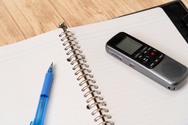 開かれたメモ帳、その上のペンとボイスレコーダー